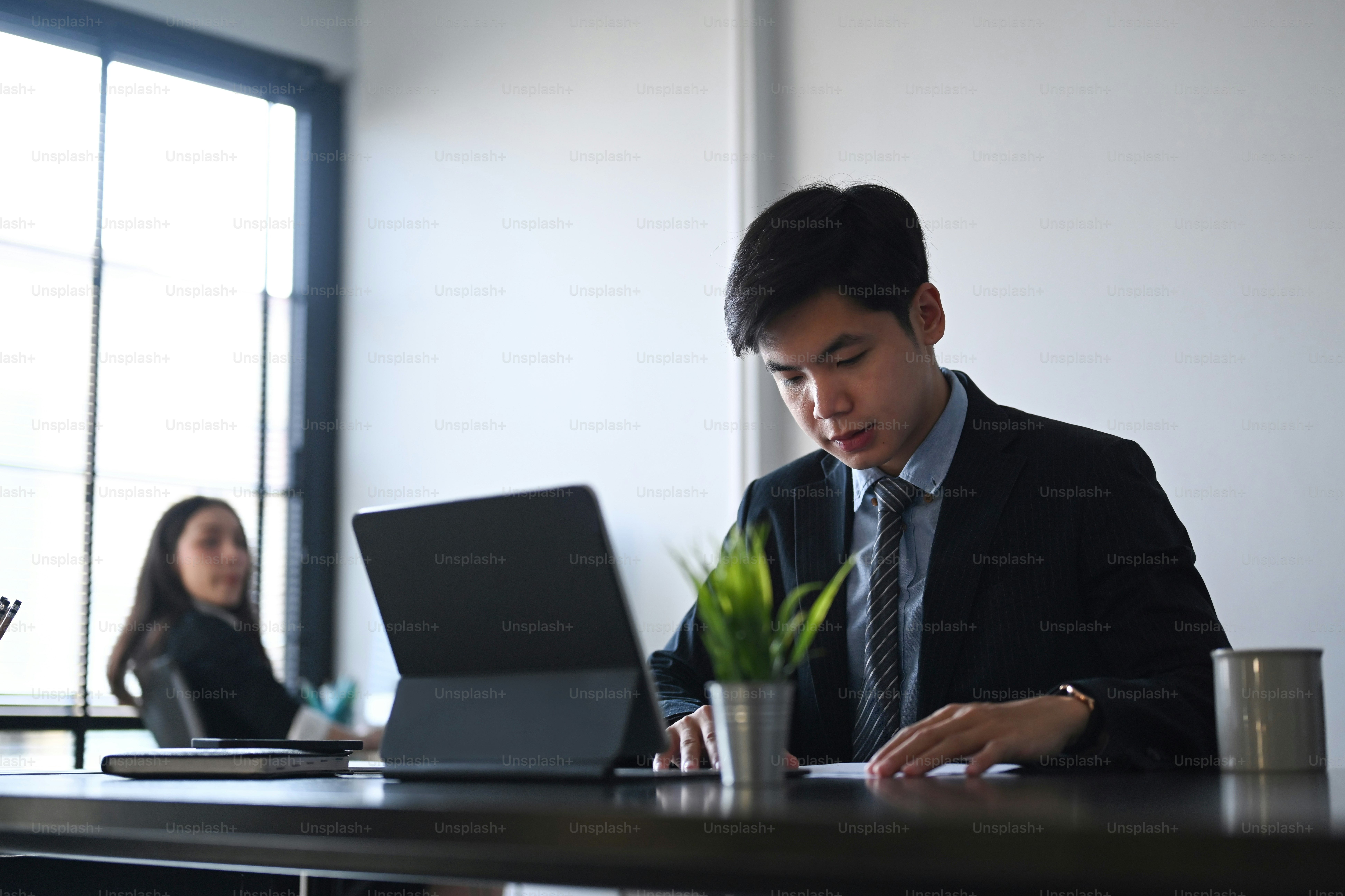 Businessman using tablet computer and concentrate analyzing business documents while sitting with his colleague in office.