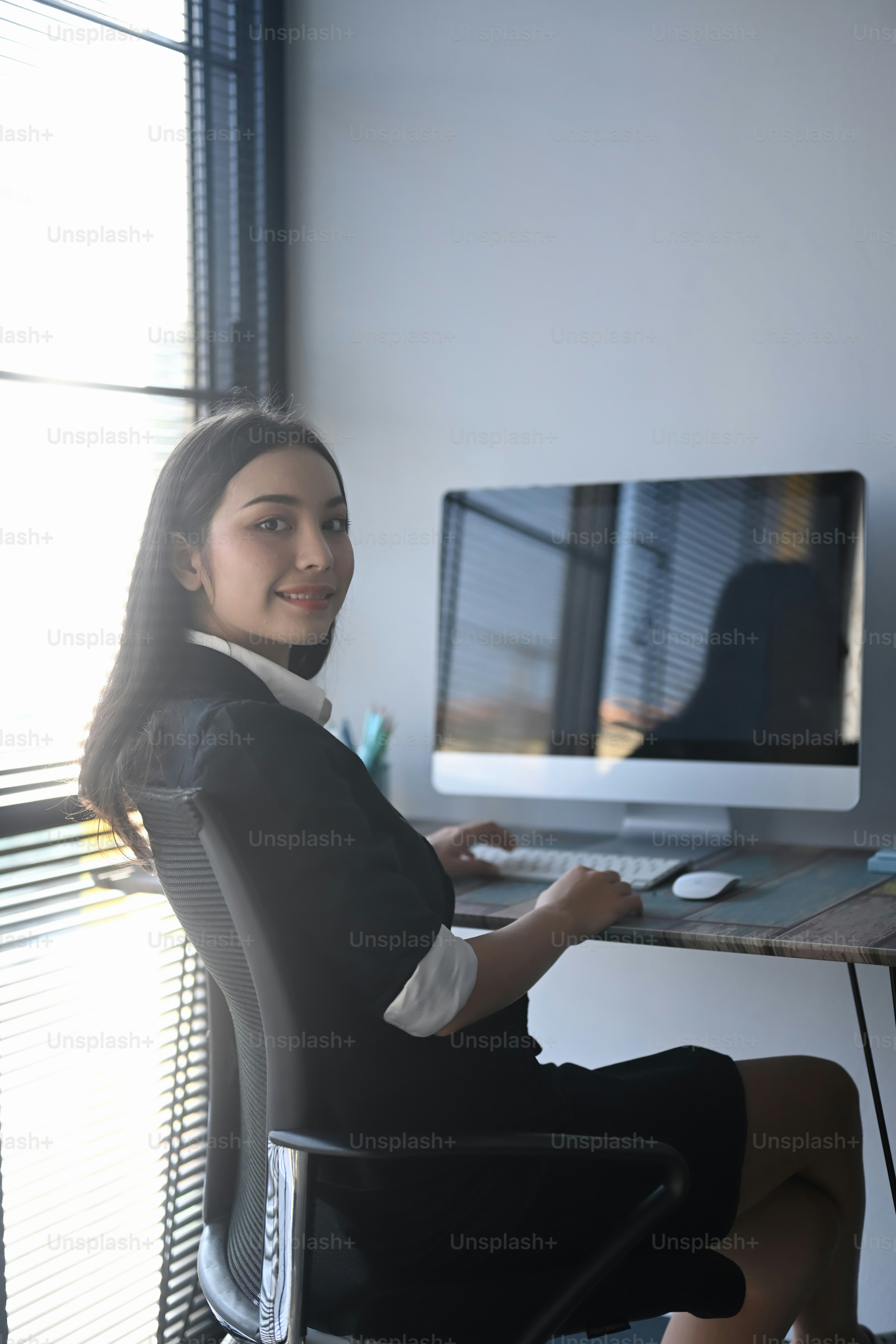 Portrait of a cheerful young woman office worker sitting at her workspace and smiling to camera.