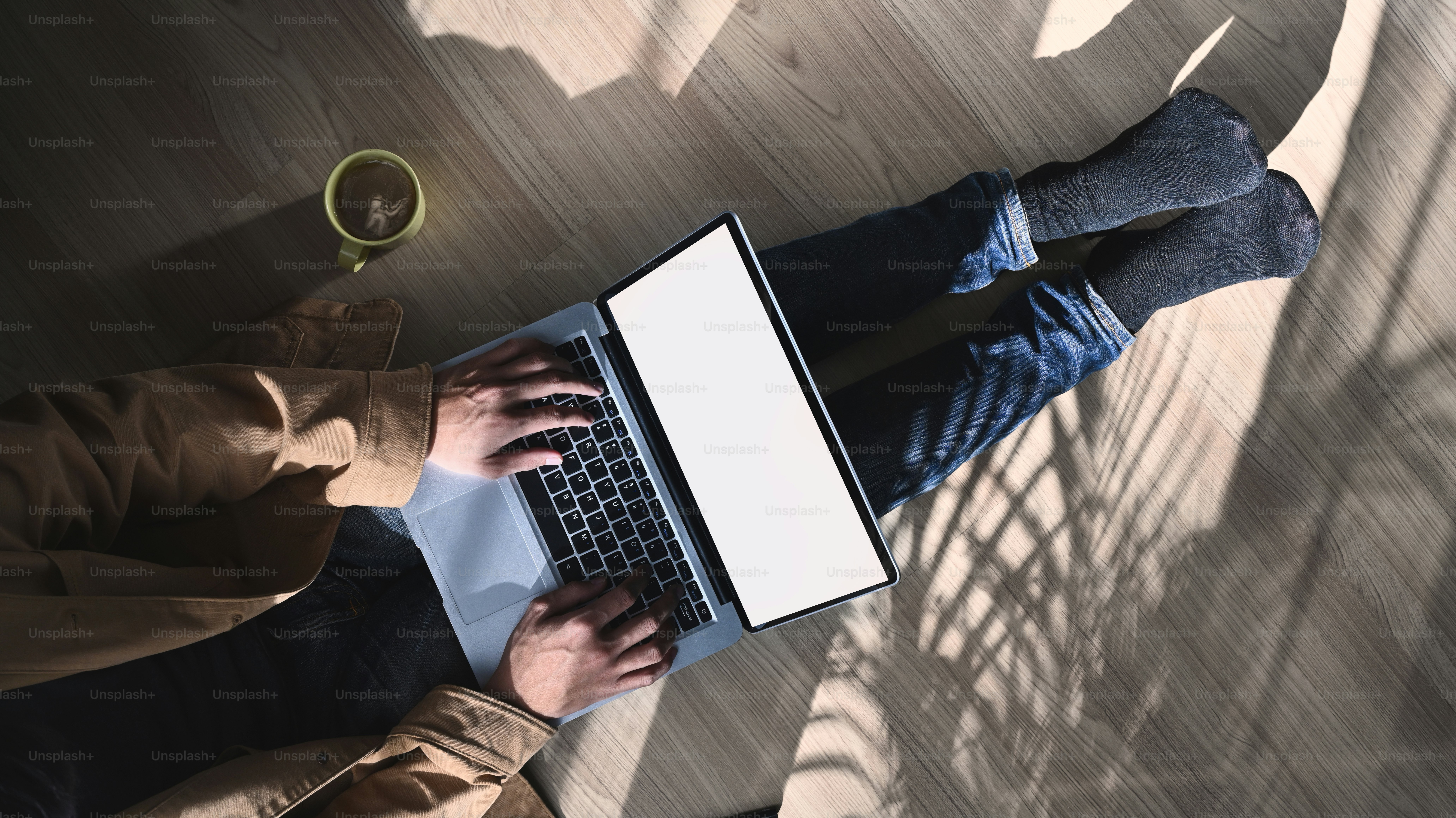 Over head shot of casual man freelancer sitting on floor and working on laptop computer with blank screen.