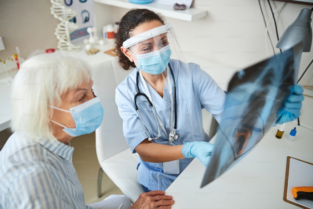 Medico con un sorriso sotto la maschera che si rende conto che la radiografia del suo paziente anziano mostra un torace sano