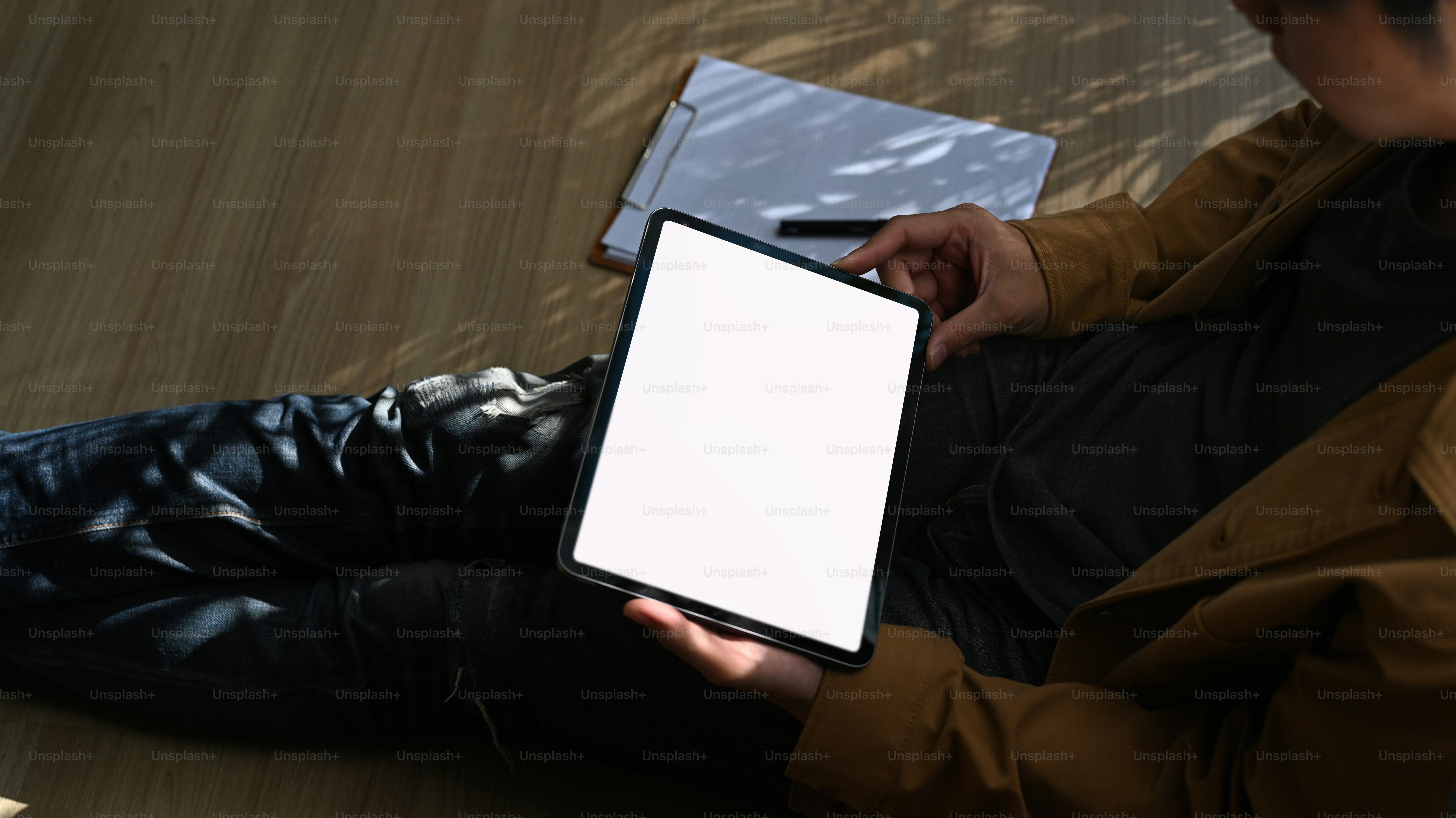 Close up view of young man hands holding digital tablet while sitting on wooden floor in living room.