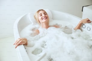 Close up portrait of charming blonde Caucasian woman lying on the hydro bath with foam in spa resort