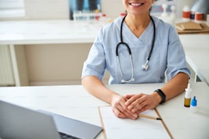 Beschnittenes Foto einer Frau in einem medizinischen Kittel mit einem Lächeln im Gesicht am Tisch