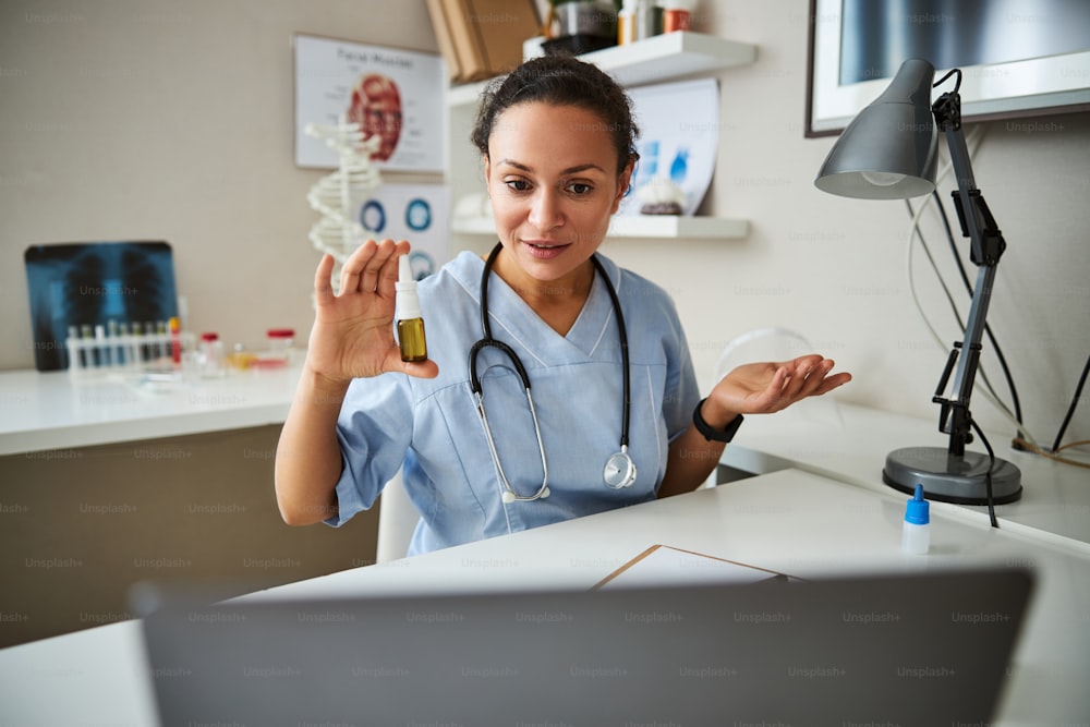 Medical worker answering the questions on an internet conference while holding a bottle of nose spray before camera