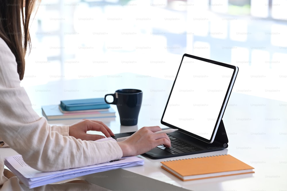 現代のオフィスで空白の画面を持つモックアップタブレットコンピューターを使用している若い女性のトリミングショット。