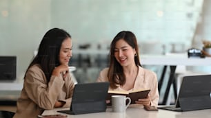 Two partners using tablet computer and talking about new ideas while sitting together in office.