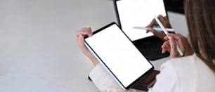 Horizontal photo of two businesswoman using mock up tablet computer while sitting in modern office.