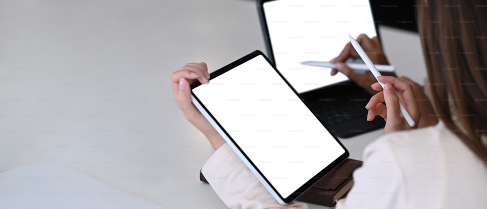 Horizontal photo of two businesswoman using mock up tablet computer while sitting in modern office.