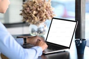 Cropped shot of young man using mock up laptop computer with blank screen at office desk.