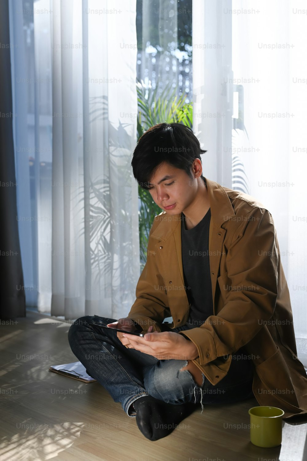 Asian man using digital tablet and sitting on wooden floor at home.