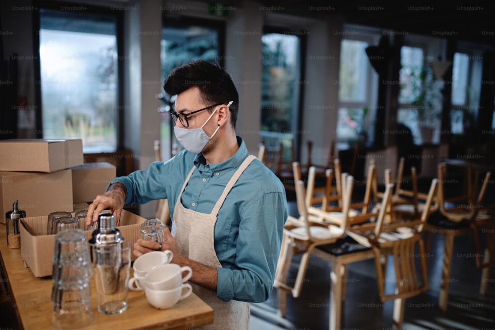 Frustrierter Kellner packt Gläser in geschlossenem Café oder Café, Lockdown für kleine Unternehmen wegen Coronavirus.