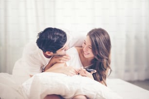 Young couple in bed, Happy smiling couple lying covered with blanket and Mobile Phone
