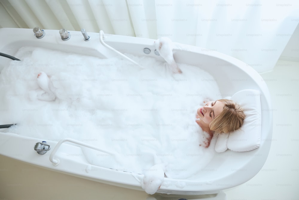 Vista superior retrato de la belleza de la mujer atractiva que usa el cuerpo relajante del spa de agua de burbujas y se acuesta en la bañera durmiendo a la hora del baño