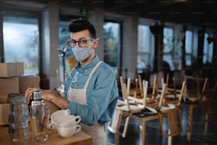 Camarero frustrado empacando vasos en una cafetería o cafetería cerrada, cierre de pequeñas empresas debido al coronavirus.