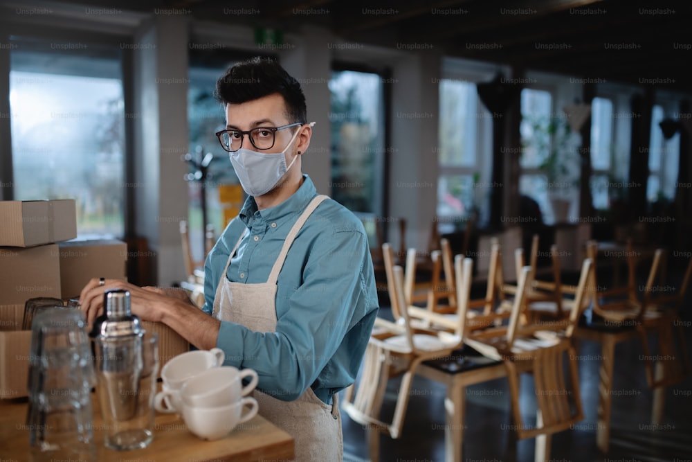 Frustrierter Kellner packt Gläser in geschlossenem Café oder Café, Lockdown für kleine Unternehmen wegen Coronavirus.
