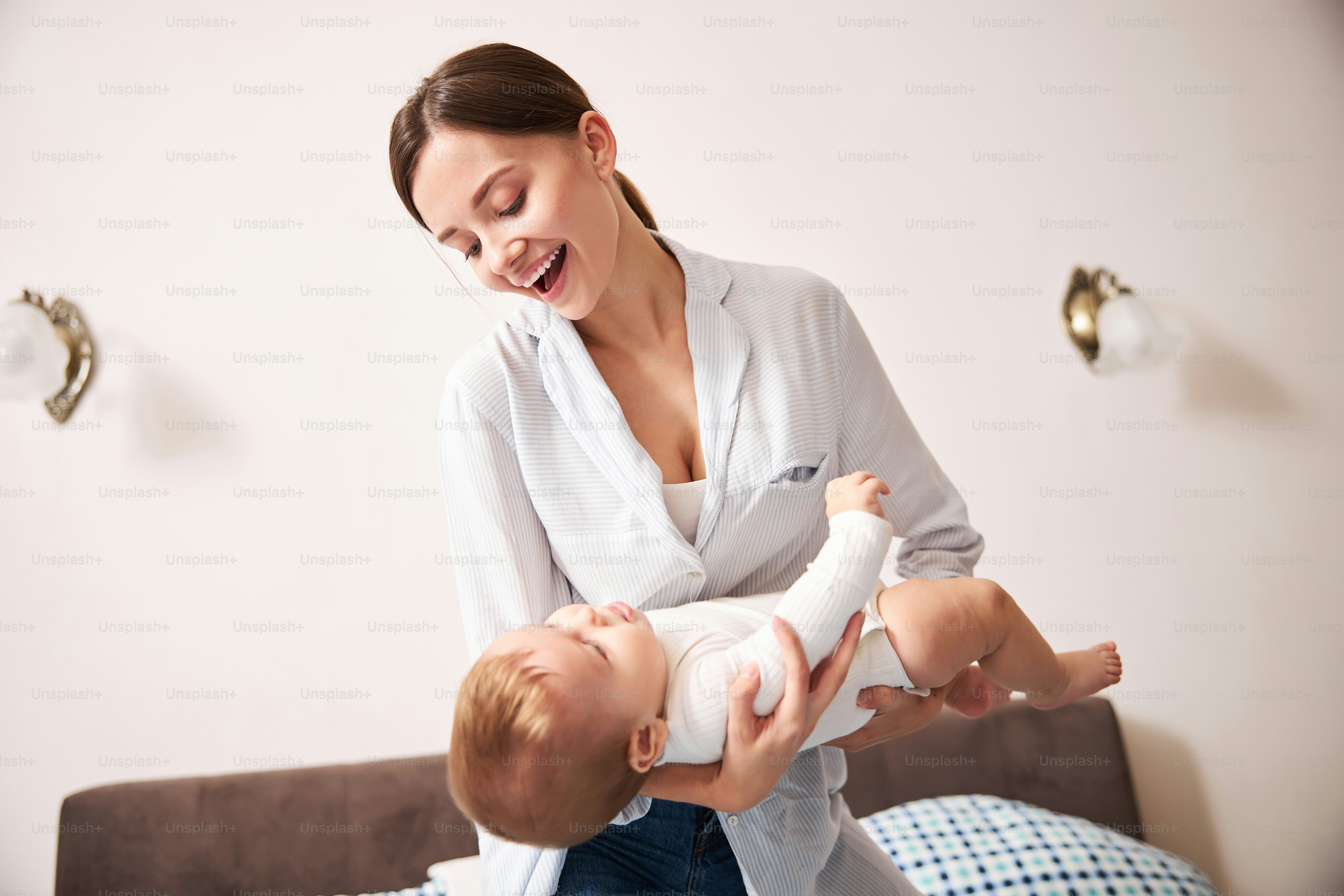 Positive delighted brunette woman keeping smile on her face while looking at her serious child