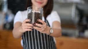 Dona de uma cafeteria de tiro cortado segurando um copo de grão de café em seu café.