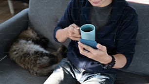 Hombre de primer plano que sufre Internet con un teléfono inteligente y sostiene una taza de café en casa.