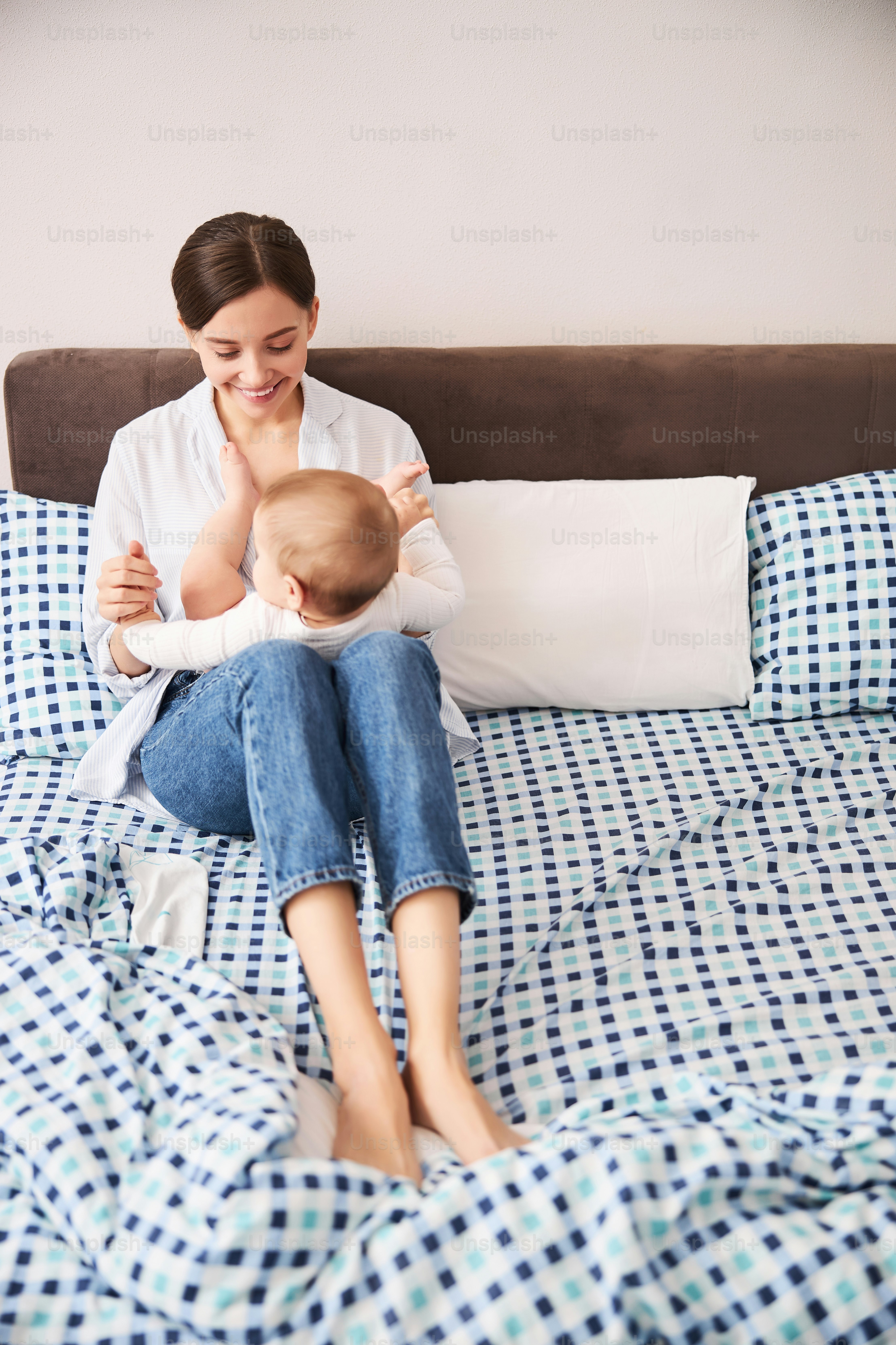Tender parent feeling happiness while sitting on the bed and looking at her kid