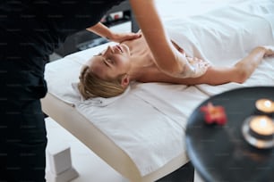 Retrato de vista lateral se elegante jovem mulher caucasiana deitada na mesa de massagem e relaxando no procedimento de aroma no resort