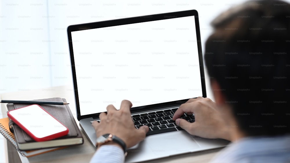 Vista de perto do empresário usando o computador portátil maquete com tela branca em sua mesa de escritório.