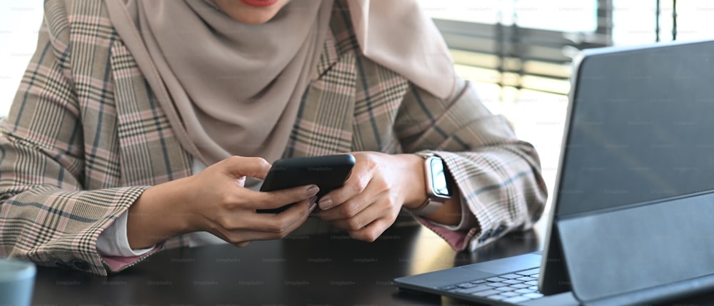 Cropped shot of muslim businesswoman in hijab using smart phone and tablet computer while sitting in office.