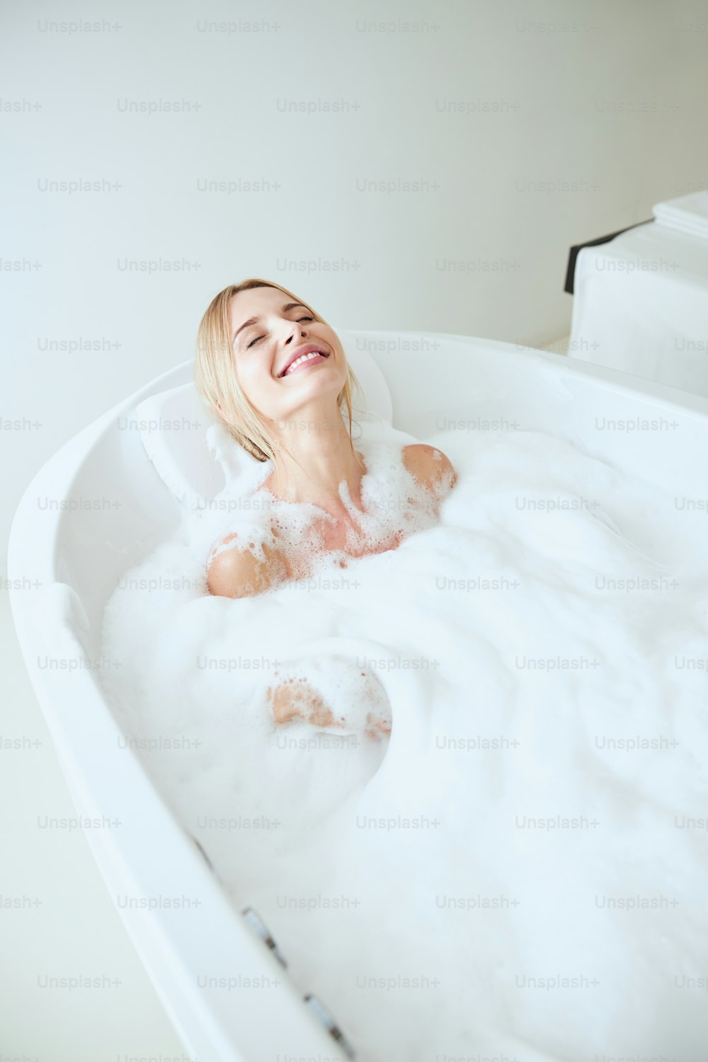 Close up portrait of happy smiling pretty woman relaxing in bath with foam in spa resort at the weekend