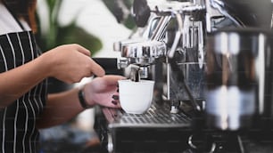 Vue rapprochée des mains du barista utilisant une machine à café pour faire du café dans le café.