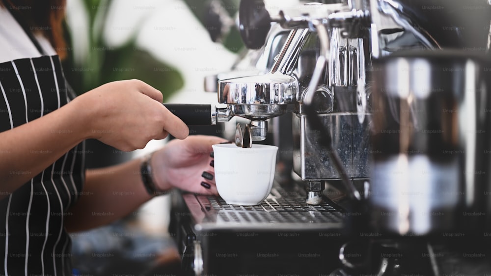 카페에서 커피를 만들기 위해 커피 머신을 사용하는 바리 스타 손의 모습을 닫습니다.