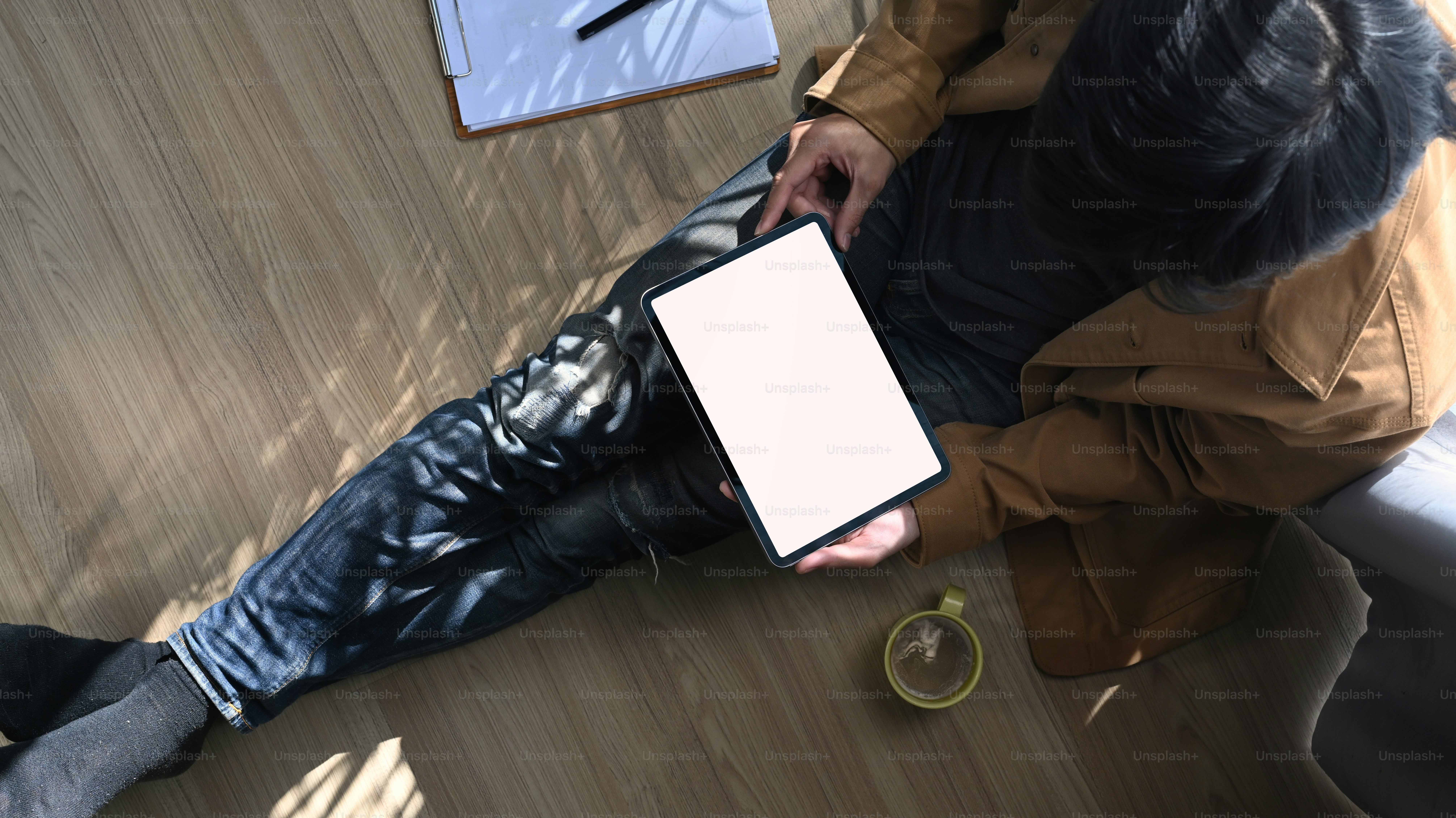 Over head shot of casual man freelancer sitting on floor and using digital tablet with blank screen.