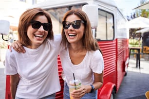 Damas de moda atentas con anteojos abrazándose mientras están de pie juntas. Concepto de amistad