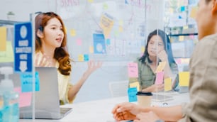 Empresários da Ásia discutindo reuniões de brainstorm de negócios compartilham dados e escrevem em divisórias de acrílico no novo escritório normal. Distanciamento social do estilo de vida e trabalho após o coronavírus.