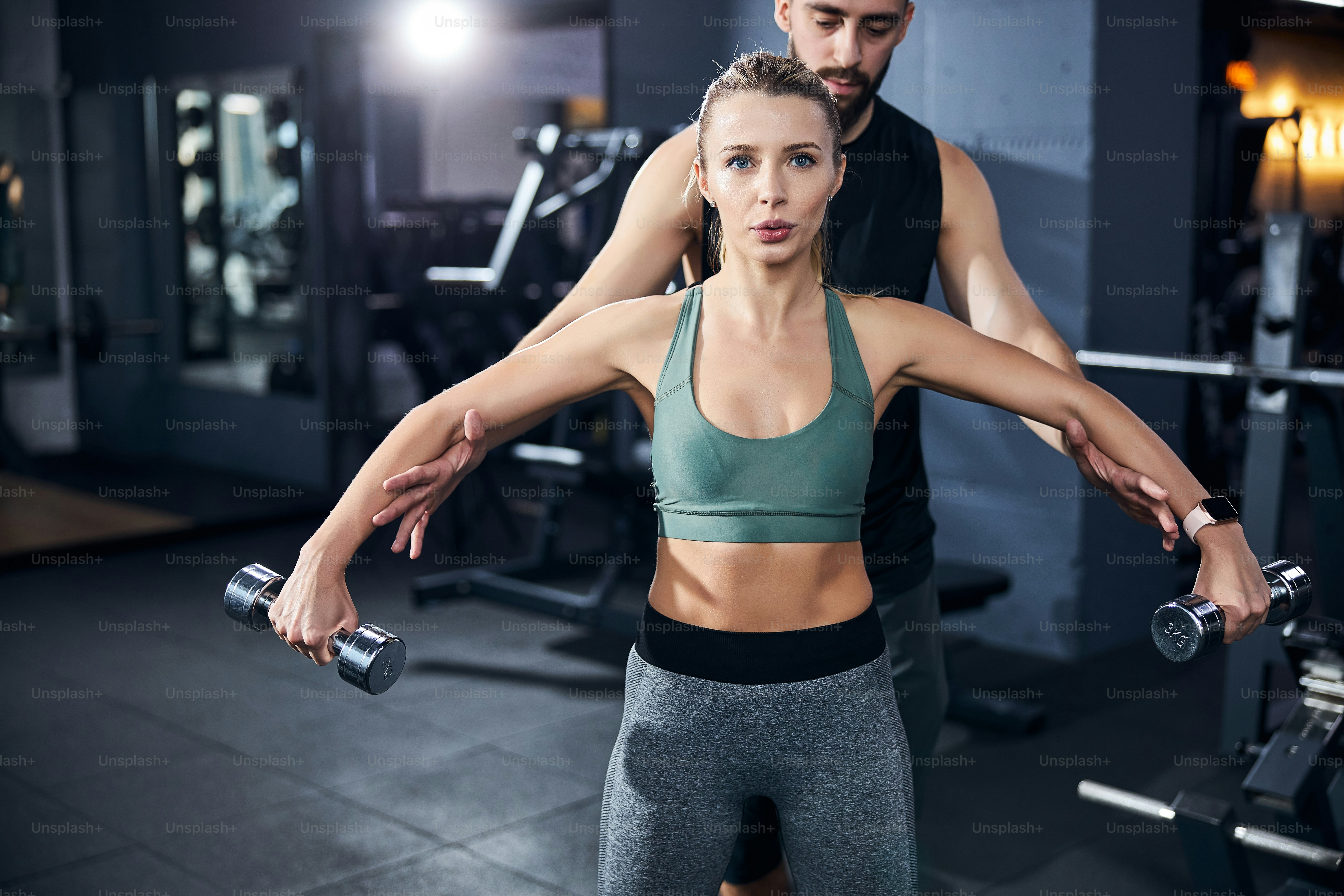 Trainer putting his hands under the arms of a woman with hand weights and raising them to a necessary level