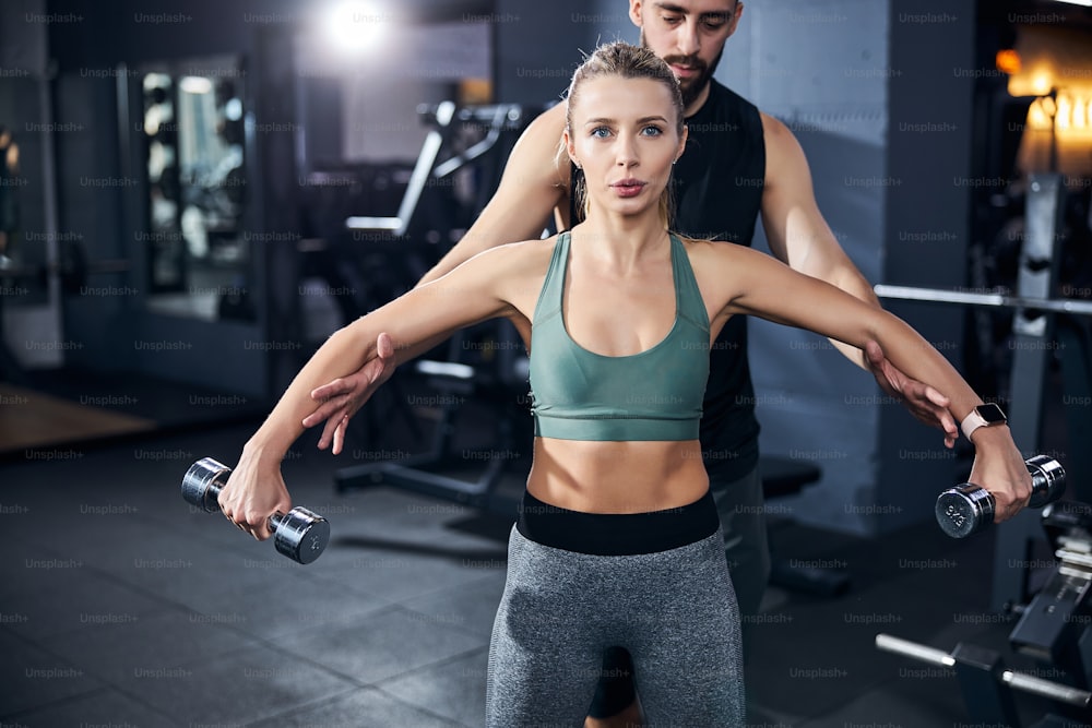 Trainer putting his hands under the arms of a woman with hand weights and raising them to a necessary level