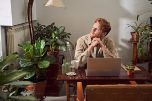 Uomo d'affari bello con i capelli rossi seduto al tavolo davanti al computer portatile aperto