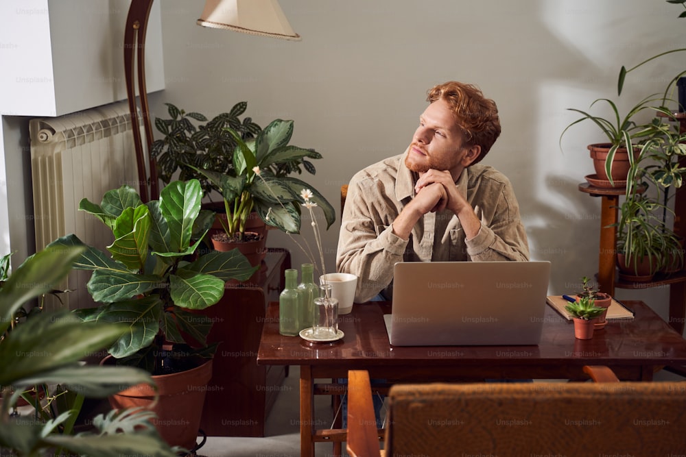 Handsome businessman with red hair sitting at table in front of open laptop