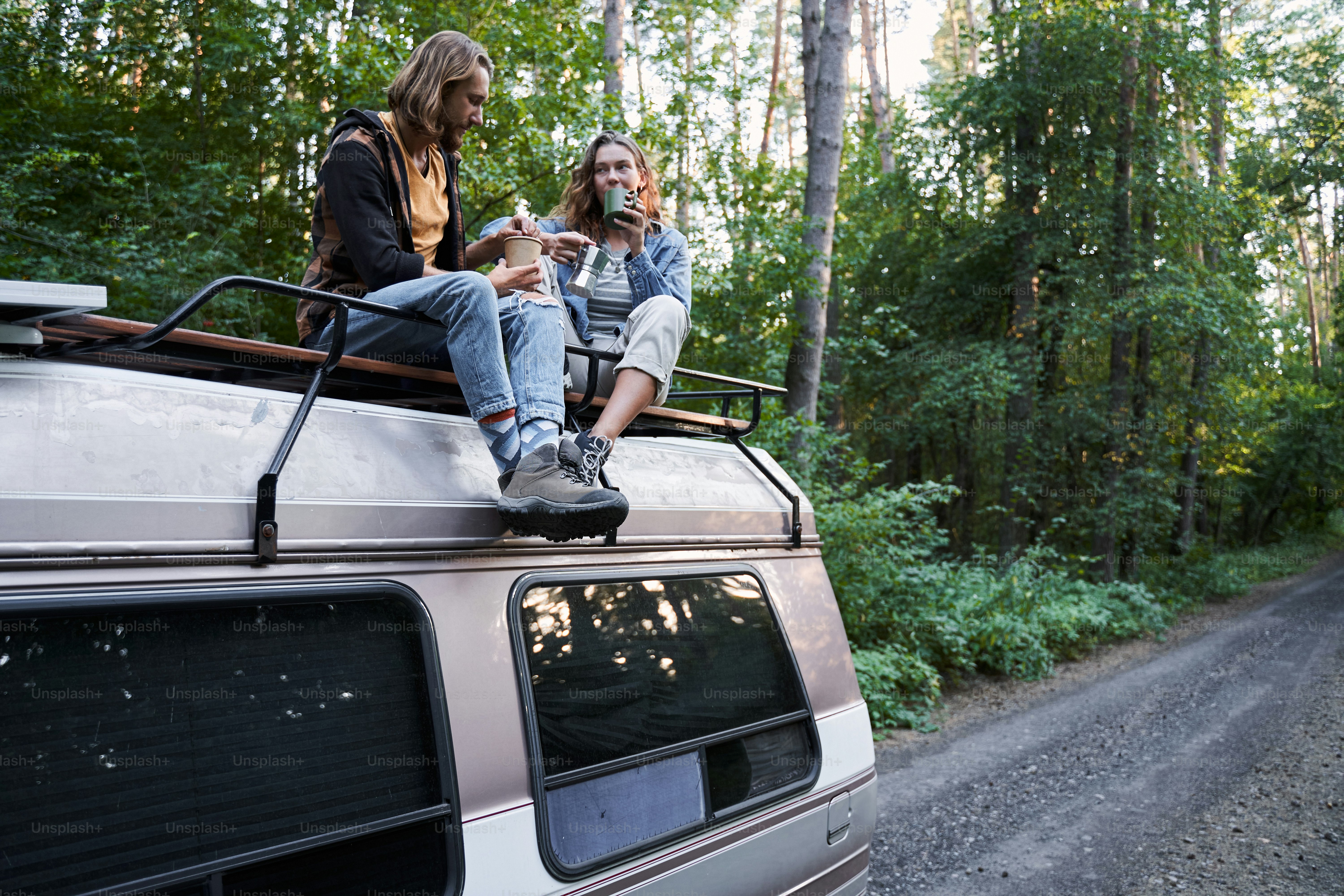 Lunch at the open air. Pleased young couple admiring each other and having lunch while sitting closely on the roof of the car