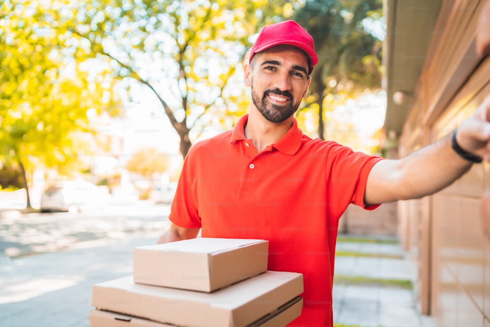 段ボールのピザの箱が家のドアベルを鳴らしている配達員の肖像画。配送および配送サービスのコンセプト。