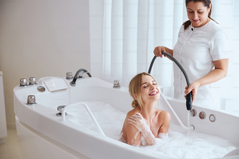 Waist up portrait of professional cosmetologist massaging woman in the bath with a jet of water in beauty salon