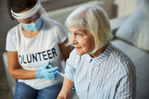 Anciana sintiendo poco dolor mientras recibe una inyección de una trabajadora social sentada a su lado