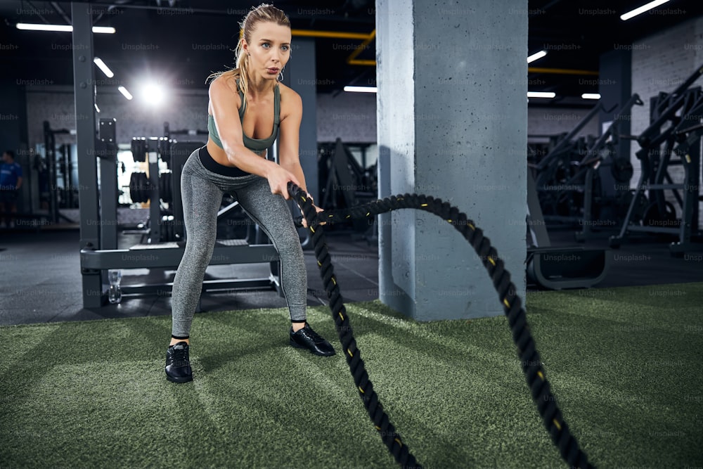 Leaned fitness enthusiast paying all her attention to using the black battling ropes correctly