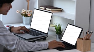 Side view of businessman working with multiple devices with blank screen at his home office.