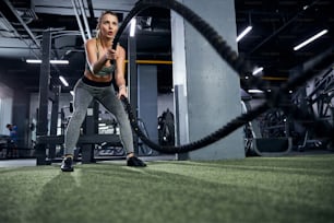 Athletic citizen making a biceps wave with a battling rope moving above the rug