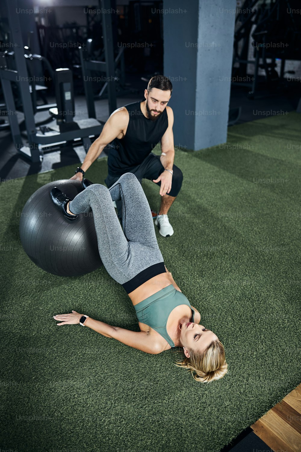 Fitness trainer maintaining an exercise ball in one place with a woman placing her feet on its top