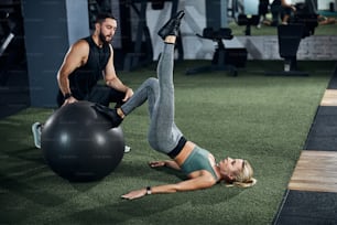 Person following the instructions of a gym coach and pulling her leg upwards during a fitness ball activity