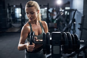 Visitante del gimnasio que vuelve a colocar un disco de fitness en el estante con otros después de completar el ejercicio con él