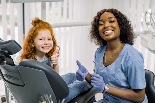 Smiling young girl patient giving thumbs up at dentist