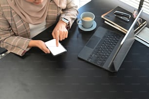 Overhead shot of muslim businesswoman in hijab using smart phone and tablet computer while sitting in her office desk.