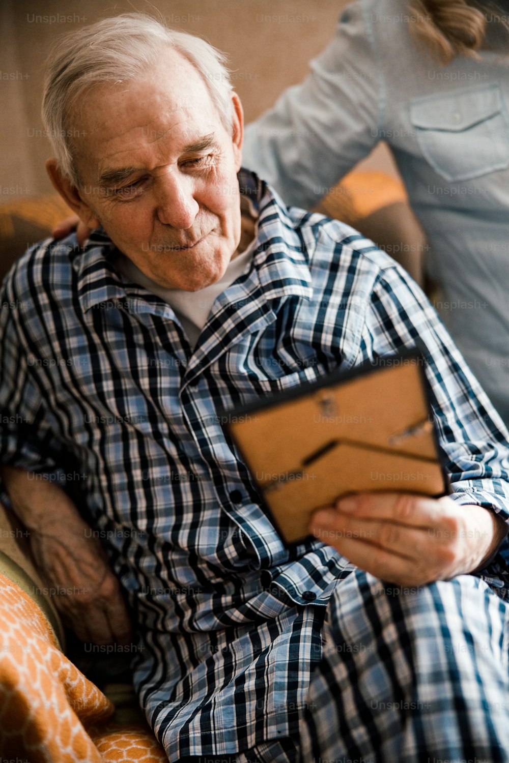 Portrait of glad elderly man looking at the photo in the frame. His wife is standing behind him and smiling
