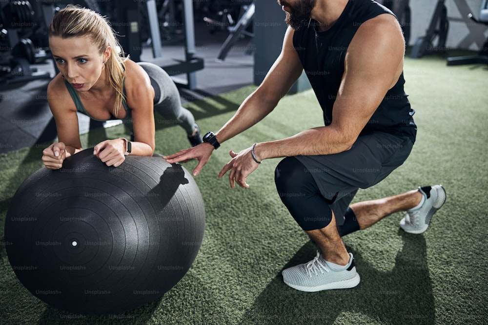 Trainer explaining the rules of an exercise to a sportsperson lying on a stability ball with her hands